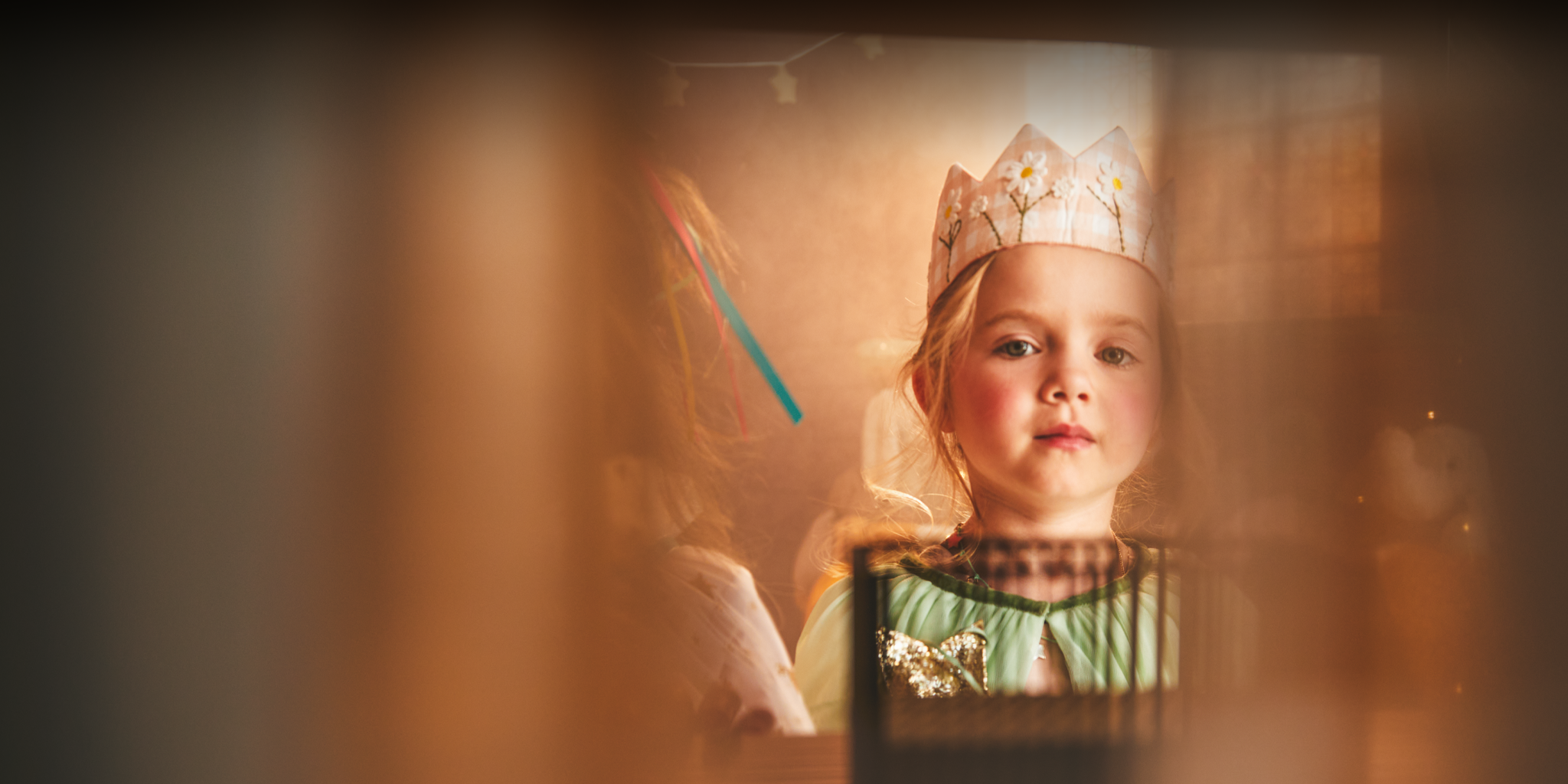 Child wearing a crown and green dress with a blurred background